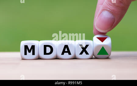 Hand dreht einen Würfel und verändert die Richtung, in die sich ein Pfeil symbolisiert, dass der Deutsche Aktienindex MDAX der Trend ändert, und geht bis statt Stockfoto