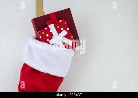 In der Nähe der traditionellen roten und weißen Plüsch Weihnachtsstrumpf mit zwei eingepackten Geschenke auf einem goldenen Haken vor einem weißen Hintergrund gefüllt Stockfoto