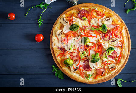 Frische italienische Pizza mit hühnerfilet, Champignons, Schinken, Salami, Tomaten, Käse auf auf schwarzem Hintergrund. Italienisches Essen. Ansicht von oben. Stockfoto