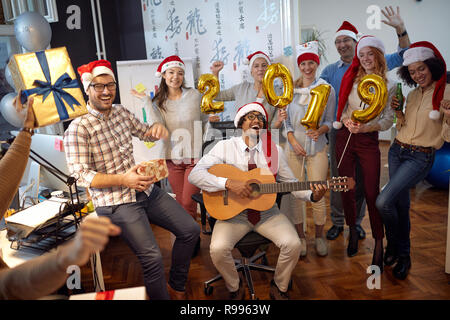 Happy business Arbeiter haben Spaß und Tanz in Santa Hut auf Xmas Party und zum Austausch der Geschenke im Büro Stockfoto