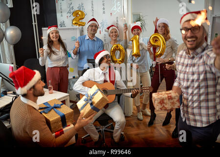 Lächelnd Business Team Spaß haben und tanzen in Santa Hut auf Xmas Party und zum Austausch der Geschenke im Büro Stockfoto