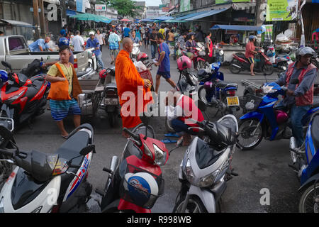 Ein Motorrad Taxi driver in den wichtigsten Markt in der Stadt Phuket, Thailand, Bögen zu einem buddhistischen Mönch und zahlt seinen Respekt mit einer traditionellen thailändischen 'Wai' Stockfoto