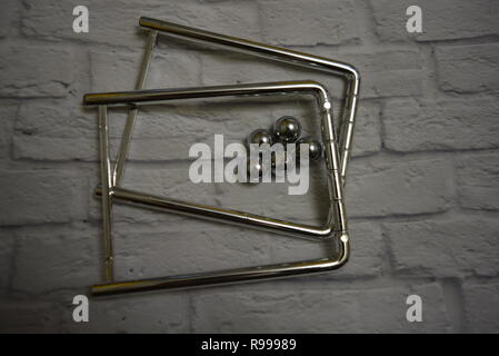 Verworrene Metallkugeln zwischen sich und Angelschnur mit Metallständern auf dem Hintergrund einer weißen Ziegelwand. Stockfoto