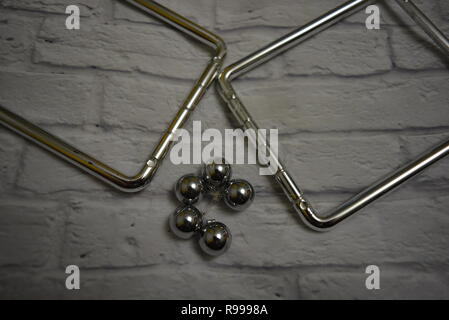 Verworrene Metallkugeln zwischen sich und Angelschnur mit Metallständern auf dem Hintergrund einer weißen Ziegelwand. Stockfoto