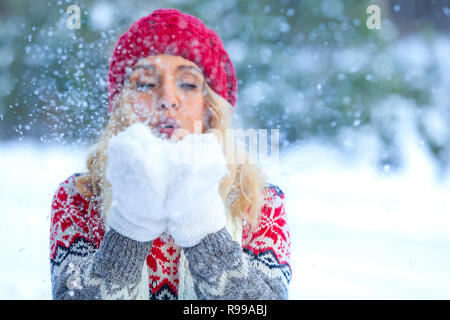 Closeup schoss der blonden Frau, die bläst Schneeflocken aus ihren Händen im Winter Wald Stockfoto