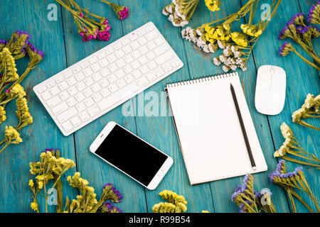 Arbeitsplatz mit wireless Slim Keyboard, Maus, Smart Phone, Notepad, bunte Blumen auf blau Schreibtisch aus Holz Stockfoto