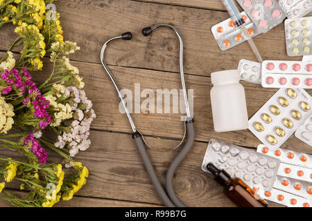 Pillen, medizinische Flasche, Spritze und Stethoskop auf braune Holztisch Stockfoto