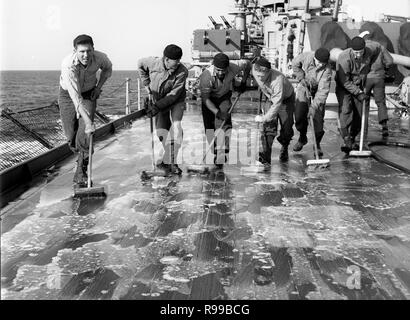 Alle Mann an Deck 1950 als US-Marine Seeleute sauber das Deck der USS Rochester (CA-124) Kreuzer Stockfoto