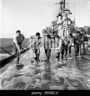 Alle Mann an Deck 1950 als US-Marine Seeleute sauber das Deck der USS Rochester (CA-124) Kreuzer Stockfoto