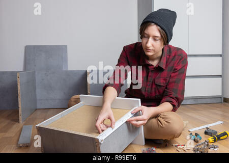 Frau Montage einer Brust Schublade für neue Schlafzimmer Möbel. Weibliche in casual Shirt und Stricken hat typische 'Men' Tischler Arbeit zu Hause Stockfoto