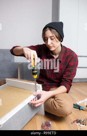 Frau Montage einer Brust Schublade für neue Schlafzimmer Möbel. Weibliche in casual Shirt und Stricken hat typische 'Men' Tischler Arbeit zu Hause Stockfoto