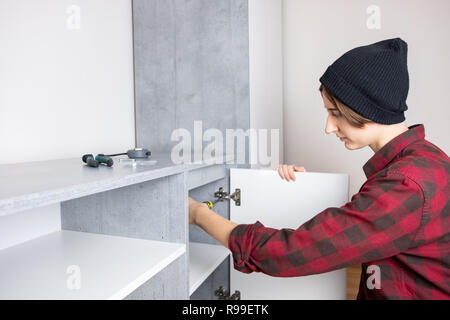 Frau einstellen Möbel Tür in einem neuen Wohnzimmer Schrank. Weibliche in casual Shirt und Stricken hat 'Men' Tischler Arbeit zu Hause Stockfoto