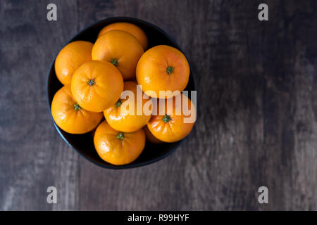 Bündel von Satsuma Orangen in einem schwarzen Schüssel auf ein Holz Hintergrund Stockfoto