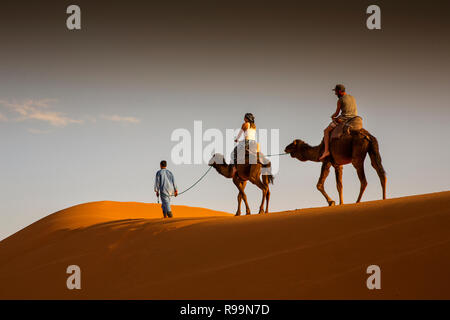 Marokko Errachidia Provinz, Erg Chebbi, Touristen auf Kamelen durch die Dünen bei Sonnenuntergang Stockfoto