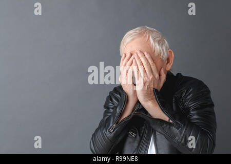Ältere Menschen tragen schwarze Lederjacke auf graue Wand isoliert, die Augen mit den Händen schreien unglücklichen close-up Stockfoto