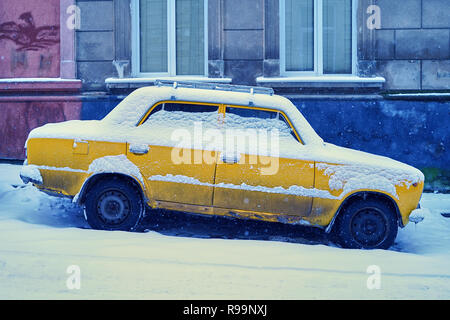 Alte schmutziges Gelb Auto mit Schnee an einem verschneiten abfallende Strasse im Winter Stadt geparkten abgedeckt Stockfoto