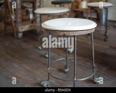 Alte vintage aus Eisen und Holz Barhocker mit Rädern mit schwarzen und weißen Stoff Polster oben auf Holzboden in Cafe Dekoration retro Style. Stockfoto