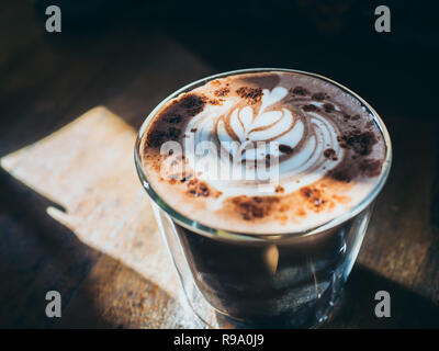 Ein Glas heiße Schokolade mit Blatt latte Art oben auf Holztisch mit schönen Licht und Schatten Stil. Stockfoto