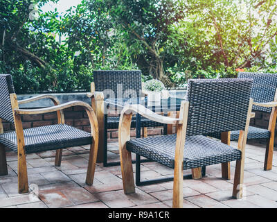 4 Outdoor Holz- und weave Sessel und Glastisch auf Stein, in der Nähe des Garten. Stockfoto