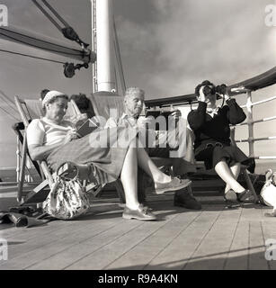 1950, historische, drei Fahrgäste, die auf der Union - Schloss Dampfschiff "Kenia" saß in Liegestühlen draußen auf Deck, zwei von ihnen Bücher zu lesen, während die weiblichen Passagiere durch ein Fernglas schaut. Stockfoto