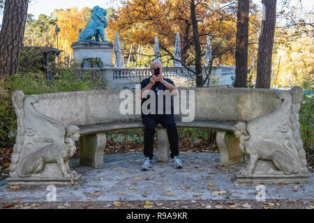 Berlin. Alte Mann sitzt auf decorartive Bank im Garten von Haus der Wannsee-Konferenz Gedenkstätte mit Flensburger Löwe im Hintergrund.. Stockfoto