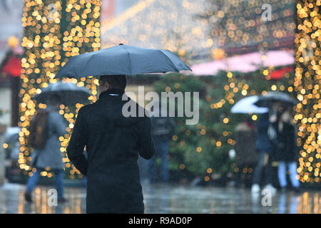 Köln, Deutschland. 21. Dezember 2018, Nordrhein-Westfalen, Köln: Besucher gehen über den Weihnachtsmarkt an der Kathedrale mit Sonnenschirmen zwischen den Ständen. Am vierten Wochenende im Advent, das Rheinland erwartet, Regen und milde Temperaturen. Foto: Henning Kaiser/dpa Quelle: dpa Picture alliance/Alamy leben Nachrichten Stockfoto