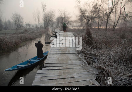 Srinagar, Indisch kontrollierten Teil Kaschmirs. 21 Dez, 2018. Eine Frau geht in Kaschmir auf einem Frost - überdachte Fußgängerbrücke als fährmann Zeilen sein Boot in den Nebenfluss der Dal Lake an einem kalten Morgen in Srinagar Stadt, der Sommer Hauptstadt von Indien kontrollierten Teil Kaschmirs, Dez. 21, 2018. Credit: Javed Dar/Xinhua/Alamy leben Nachrichten Stockfoto