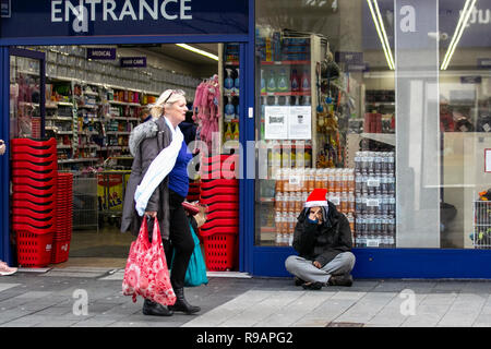 Southport Town Center, Merseyside, Großbritannien. Dezember 2018. Menschen, die an obdachlosen, raggregten Männern vorbeiziehen und Weihnachten Weihnachtsmann mit rotem Hut tragen. Kredit: MediaWorldImages/Alamy Live News Stockfoto