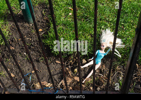 Verlorene Puppe liegend hinter einem Zaun im Park Stockfoto