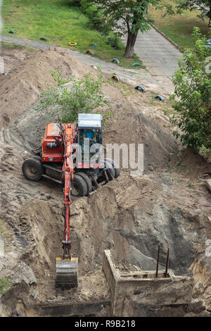 Rote Bagger gräbt eine Grube. Reparatur von Wasserleitungen. Stockfoto