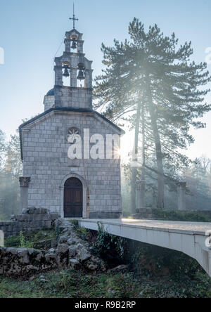 Christlich-orthodoxen Hof Kirche Cipur in Cetinje. Morgen, mit Nebel und Frost, mit Strahl der Sonne strahlt in Richtung Kirche und Baum und ein Sun Burst Stockfoto