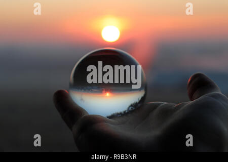 Hand mit einem Kristall Fotografie Ball reflektiert eine orange rosa Sunrise Stockfoto