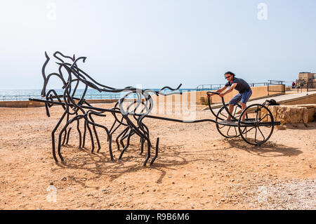 Caesarea, Israel - 22. Mai 2012: Touristische Mann stand auf moderne Skulpturen der römischen Pferd Wagen gemacht aus schwarz gebogen geschmiedete Metallständer auf alten Caes Stockfoto