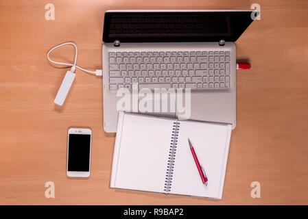 Business moderne Technologie auf dem Schreibtisch: Öffnen Sie den Laptop mit ladeleistung Bank und Memory Stick angeschlossen, Mobiltelefon und Notebook mit roter Stift Stockfoto