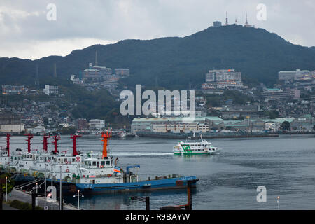 Nagasaki, Japan - 23. Oktober 2018: Nagasaki Hafen mit Fähren und cruiseboats umgeben von Bergen in der Dämmerung Stockfoto