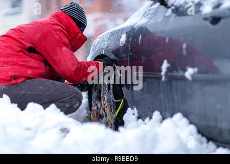 Schneeketten auf die Räder des Autos. Junger Mann vorbereiten Auto im Winter Tag unterwegs. Stockfoto