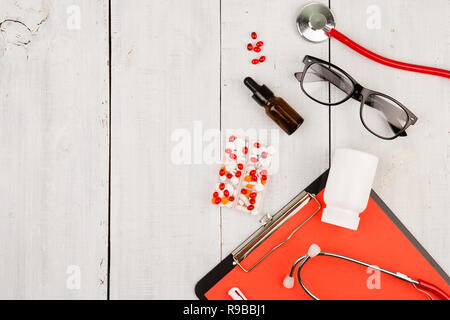 Arbeitsplatz eines Arztes. Red Stethoskop, Zwischenablage, Gläser und Pillen auf weiße Holztisch Stockfoto