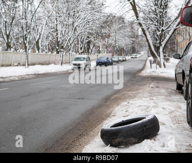 Gebrochene Auto Rad Reifen neben Straße. selektive Fokus auf Reifen, Hintergrund Straße mit Autos verwischt. outdoor Winter geschossen Stockfoto