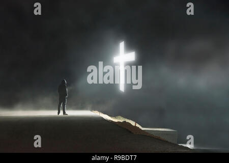 Ein Konzept der digitalen Kunst Bild eines einsamen hooded Abbildung lstanding auf einer Straße in einem leuchtenden Kreuz im Himmel schweben auf einer nebligen, dunklen Nacht suchen Stockfoto
