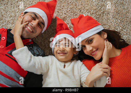 Junge Eltern, die mit ihrer kleinen Tochter unter Weihnachtsbaum unter Lügen präsentiert Stockfoto