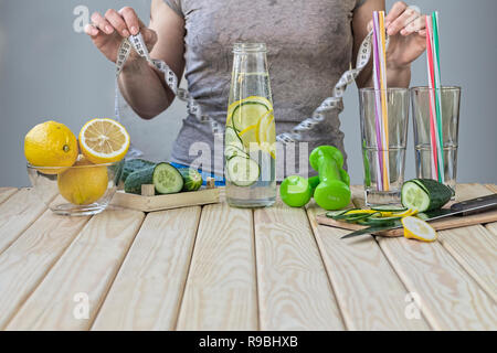 Frau Maßnahmen ihre Taille zu Hause in der Küche. Detox Drink von Gurken und Zitronen, Hanteln für Fitness. Konzept: Gesunder Lebensstil Stockfoto