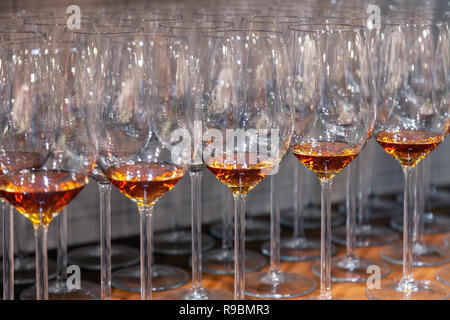 Viele Transparente crystal Weingläser mit Cognac stehen in der Zeile auf der braunen Holzfachböden in das Rack ein. Von der Seite. Konzept der Degustation Spirituosen: whi Stockfoto