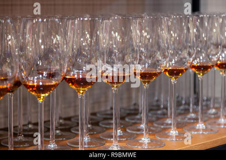 Viele Transparente crystal Weingläser mit Cognac stehen in der Zeile auf der braunen Holzfachböden in das Rack ein. Von der Seite. Konzept der Degustation Spirituosen: whi Stockfoto