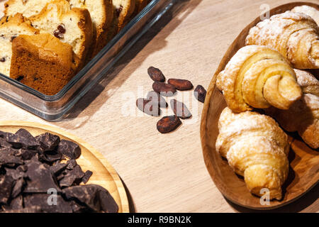 Nahaufnahme von Süßigkeiten und Gebäck und frischen Backwaren- keks Plätzchen, Kekse, Stücke von dunkler Schokolade, Rosinen, Croissants bestreut mit Puderzucker sug Stockfoto