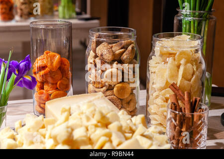 Closeup Snacks, frische Blumen lila Iris, getrocknete Früchte: Feigen, Birnen, Aprikosen in Glasvasen, Stück Käse Parmesan, Zimtstangen. Konzept degust Stockfoto