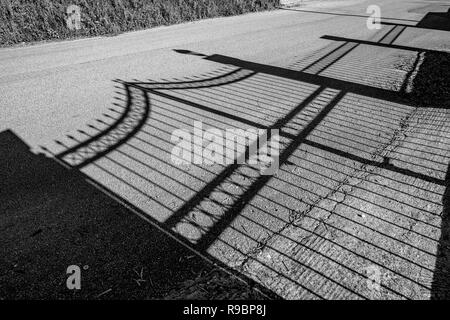 Schatten der schönen schmiedeeisernen Gartenzaun auf staubigen öffentliche Straße im Frühjahr Nachmittag in Korfu, Griechenland. Schwarze und weiße Reisen Bild Stockfoto