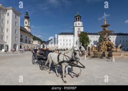 Touristen mit einer Pferdekutsche vor der Residenzbrunnen Brunnen und St. Michaels Kirche auf Residenz, Salzburg, Österreich. Stockfoto