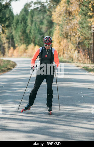 Training ein Athlet auf der Walze Skater. Biathlon Fahrt auf dem Roller Ski mit Skistöcke, im Helm. Herbst Training. Roller Sport. Stockfoto