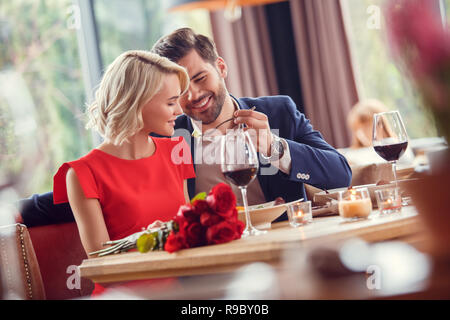 Junger Mann und Frau am Tag im Restaurant am Tisch Kerl holding Gabel mit Salat füttern Dame lächelnd verspielten Sitzen Stockfoto