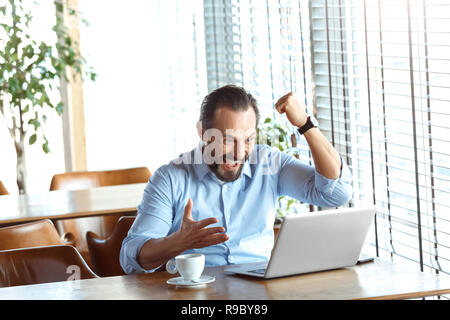 Reifer mann Händler am Tisch im Cafe am Tag sitzen bei einer Tasse Kaffee im Laptop Bildschirm Hand in Hand bis Erfolg glücklich lächelnd erreicht. Stockfoto